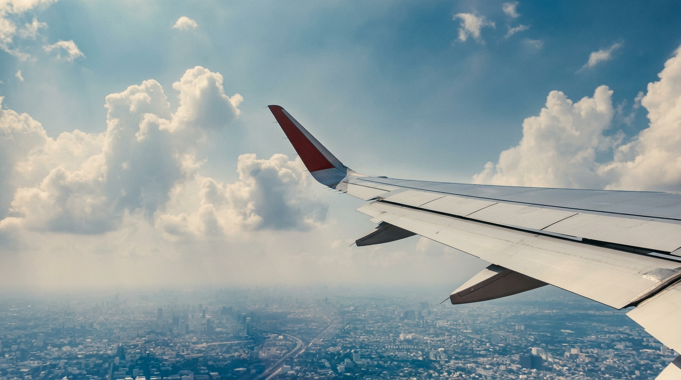 An aircraft wing above clouds and a distant city